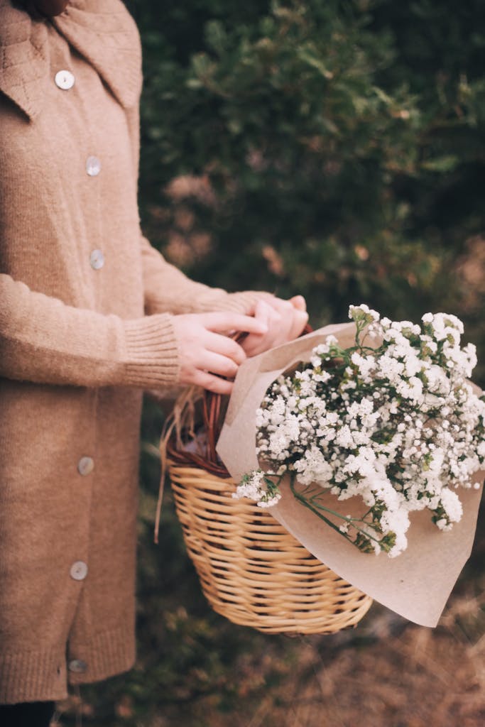 Person holding a wicker basket with white flowers in an autumn setting.